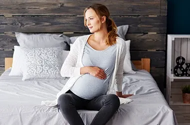 Pregnant person sitting on a bed, holding their belly.